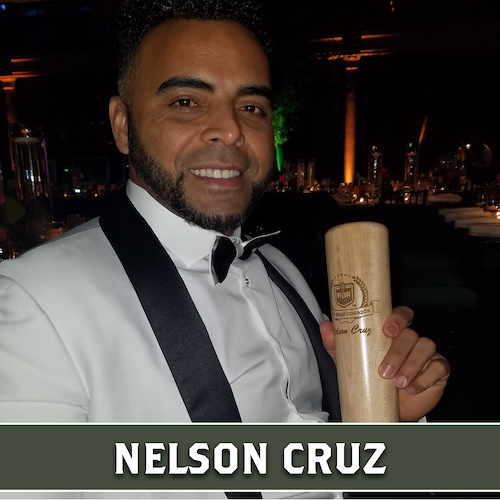 Nelson Cruz wearing a white tuxedo jacket and holding a wooden Dugout Mugs baseball bat mug.